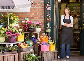 woman small business owner stands in the doorway to her flower shop