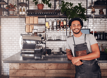 business owner wearing an apron stands in front of his bar